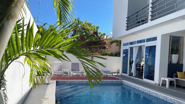 Una piscina con borde de azulejos, rodeada por un muro blanco y un ventanal que da a un balcón.