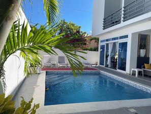A swimming pool with a tiled edge, surrounded by a white wall and a glass door leading to a balcony. - Gaia Residence (Puerto Plata)