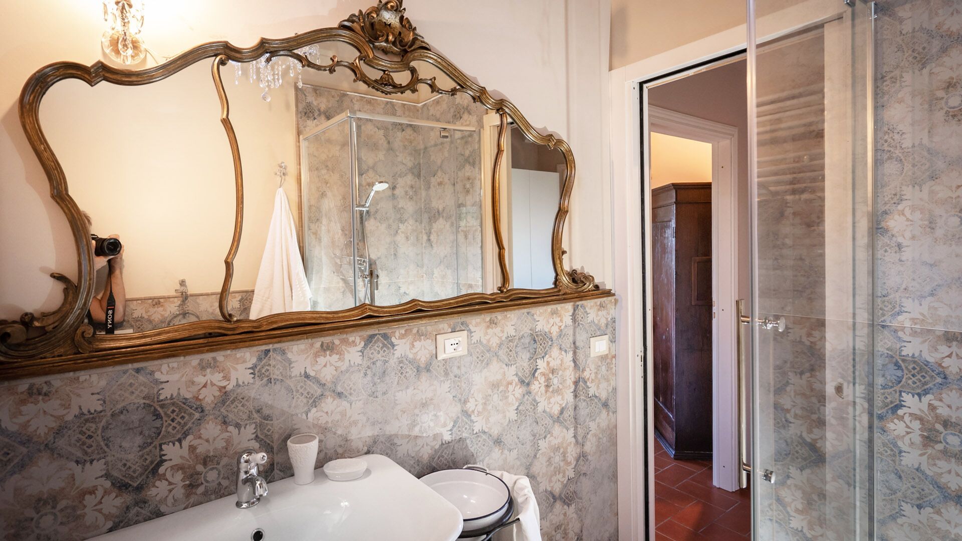 Un baño con un espejo grande y ornamentado, un lavamanos y una ducha.