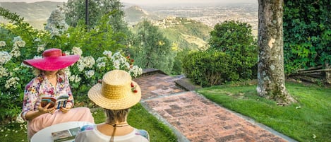 Two people sitting on a bench in a garden with a brick pathway and a view of a city in the background.