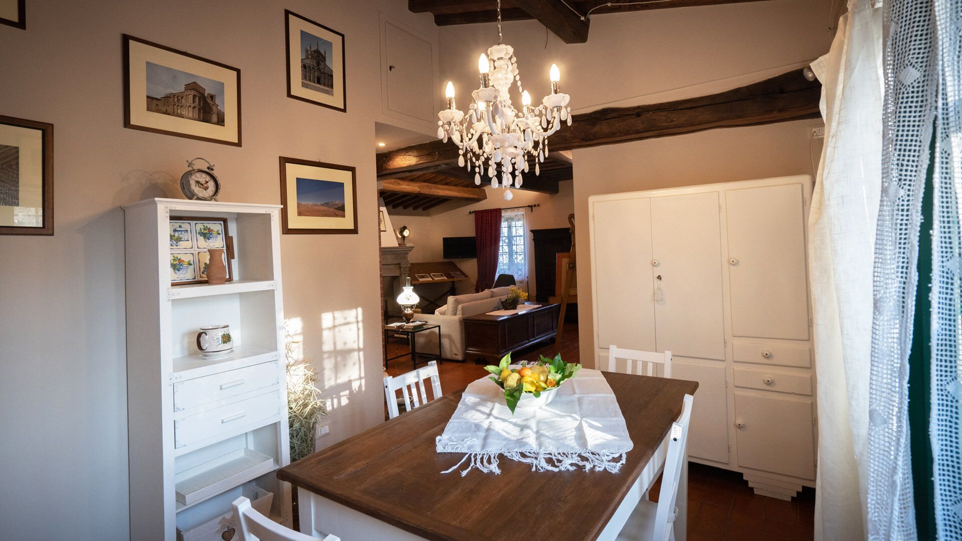 A dining area with a wooden table, white chairs, a chandelier, and framed pictures on the walls.
