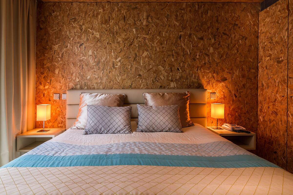 A hotel room with a wooden wall, a bed with patterned pillows, and bedside lamps.
