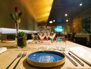A dining table set with a blue plate, wine glasses, and a rose in a vase. - Encosta do Paraiso - Apartamentos Turisticos (Guimarães)