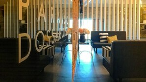A modern lobby with a central column, black sofas, and a decorative wall with vertical panels. - Encosta do Paraíso – Apartamentos Turísticos (Guimarães)