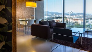 A modern living room with a large window, a dining area, and a sofa. - Encosta do Paraíso – Apartamentos Turísticos (Guimarães)