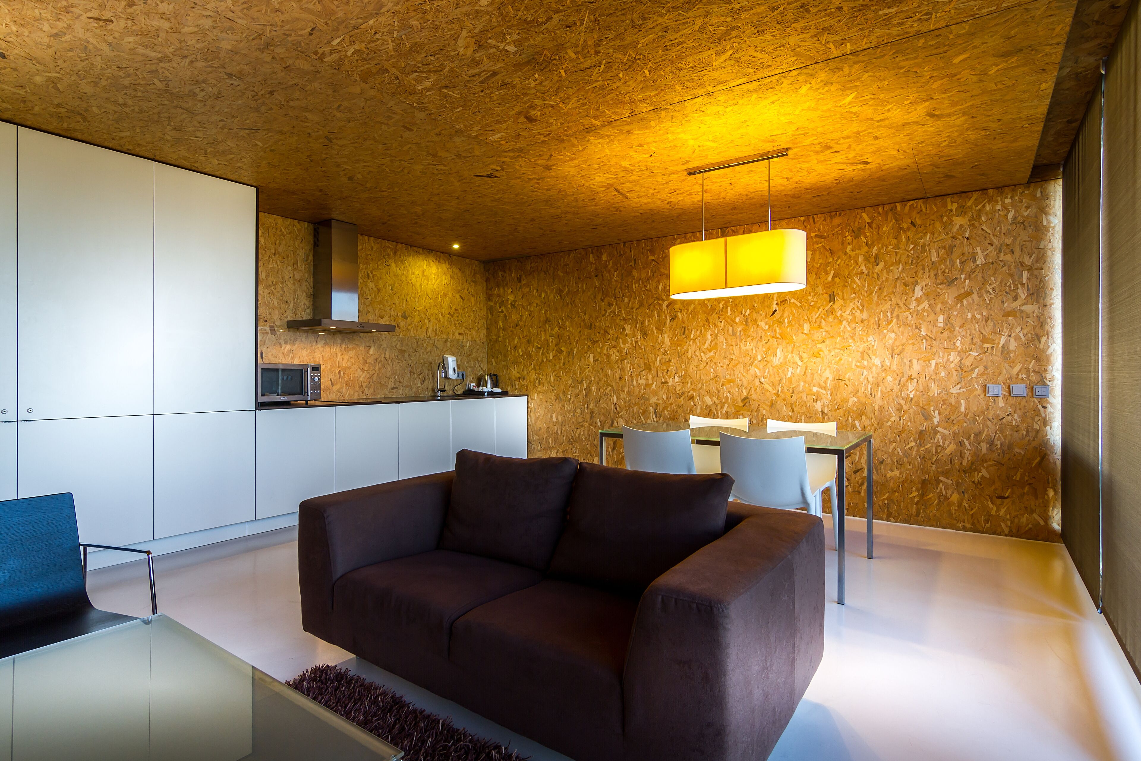 A modern living room with a brown sofa, a glass coffee table, and a dining area with a table and chairs.