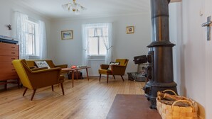 A cozy living room with wooden flooring, a vintage stove, and two armchairs. - Original North Country House (Laugar)