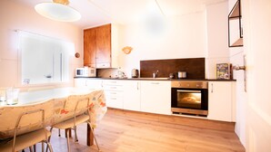 A modern kitchen with wooden cabinets, a built-in oven, a microwave, and a dining area with a table and chairs. - Original North Country House (Laugar)