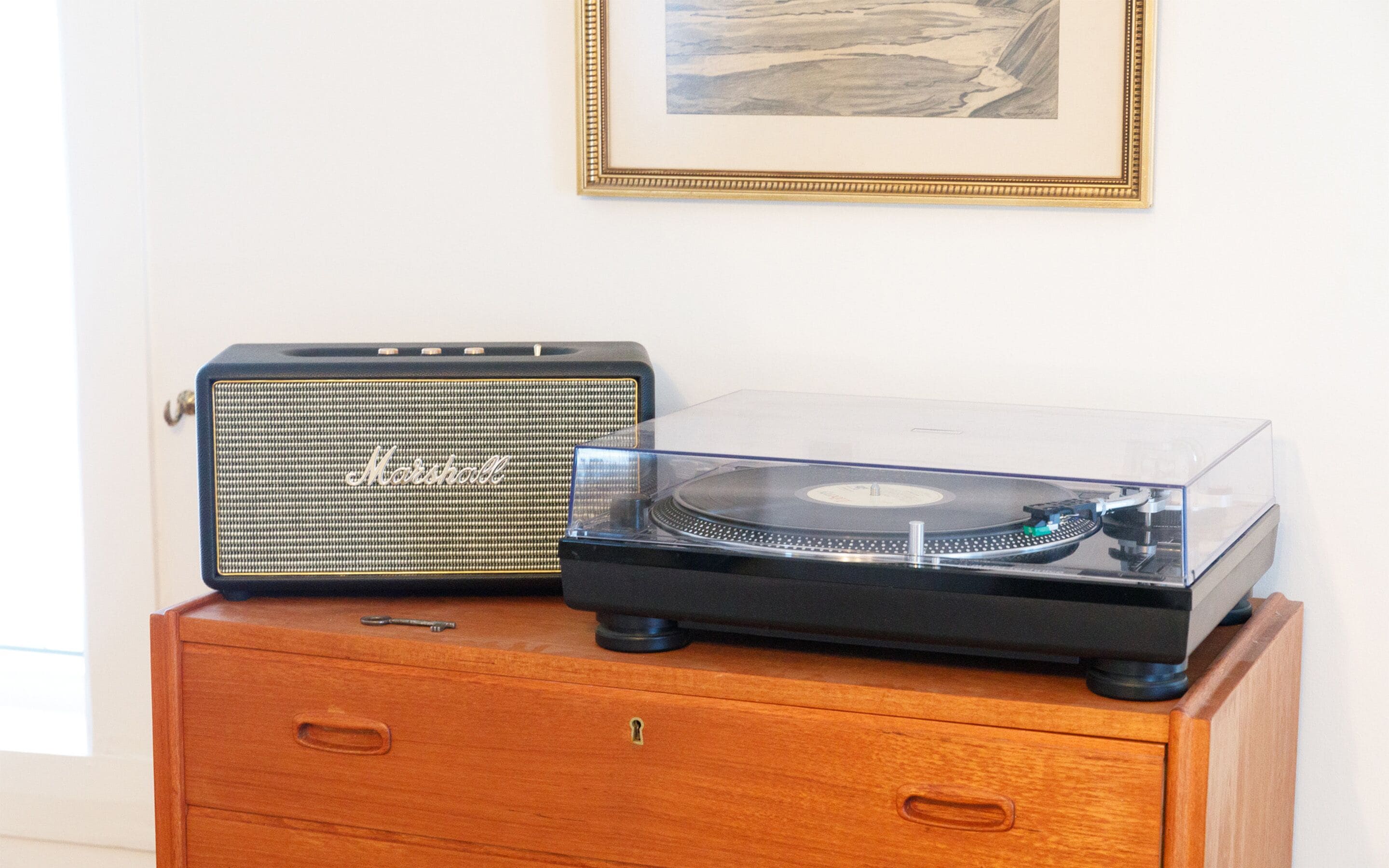 Un amplificador Marshall antiguo y un tocadiscos transparente sobre un mueble de madera.
