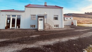 A two-story metal building with a red roof, a front door, and a small porch area. - Original North Country House (Laugar)
