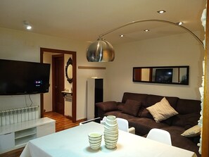 A living room with a flat-screen TV, a brown sofa, a white table with decorative bowls, and a modern pendant light. - Modern 1st line apartment in Sant Llorenç de Montgai_ WhiteHouse_ Lleida (Sant Llorenç de Montgai)