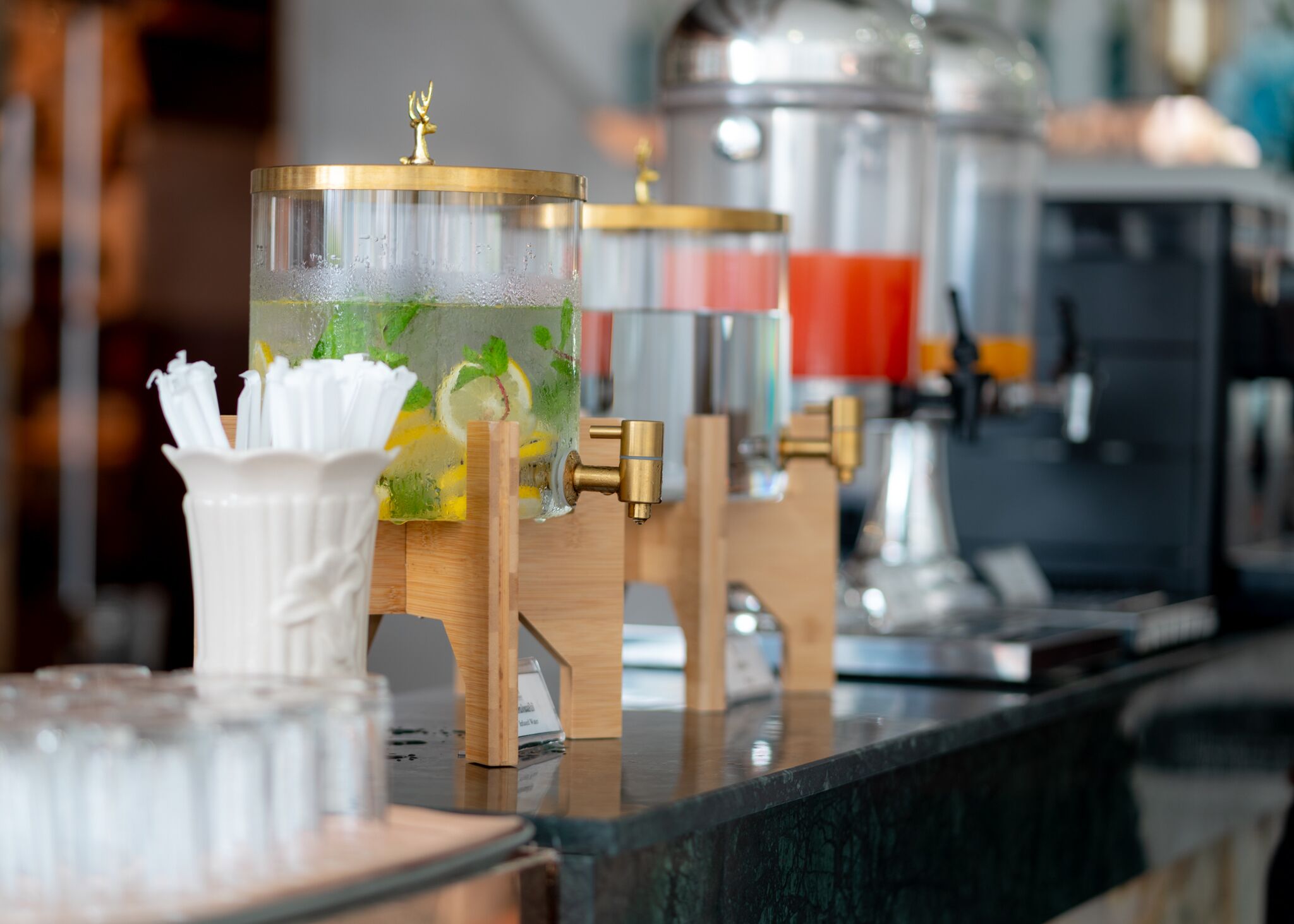 A bar area with a glass container holding a beverage, a white napkin holder, and a coffee machine in the background.