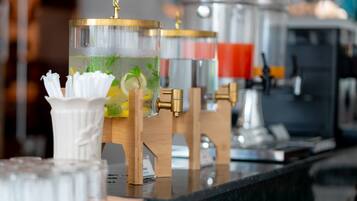 A bar area with a glass container holding a beverage, a white napkin holder, and a coffee machine in the background.