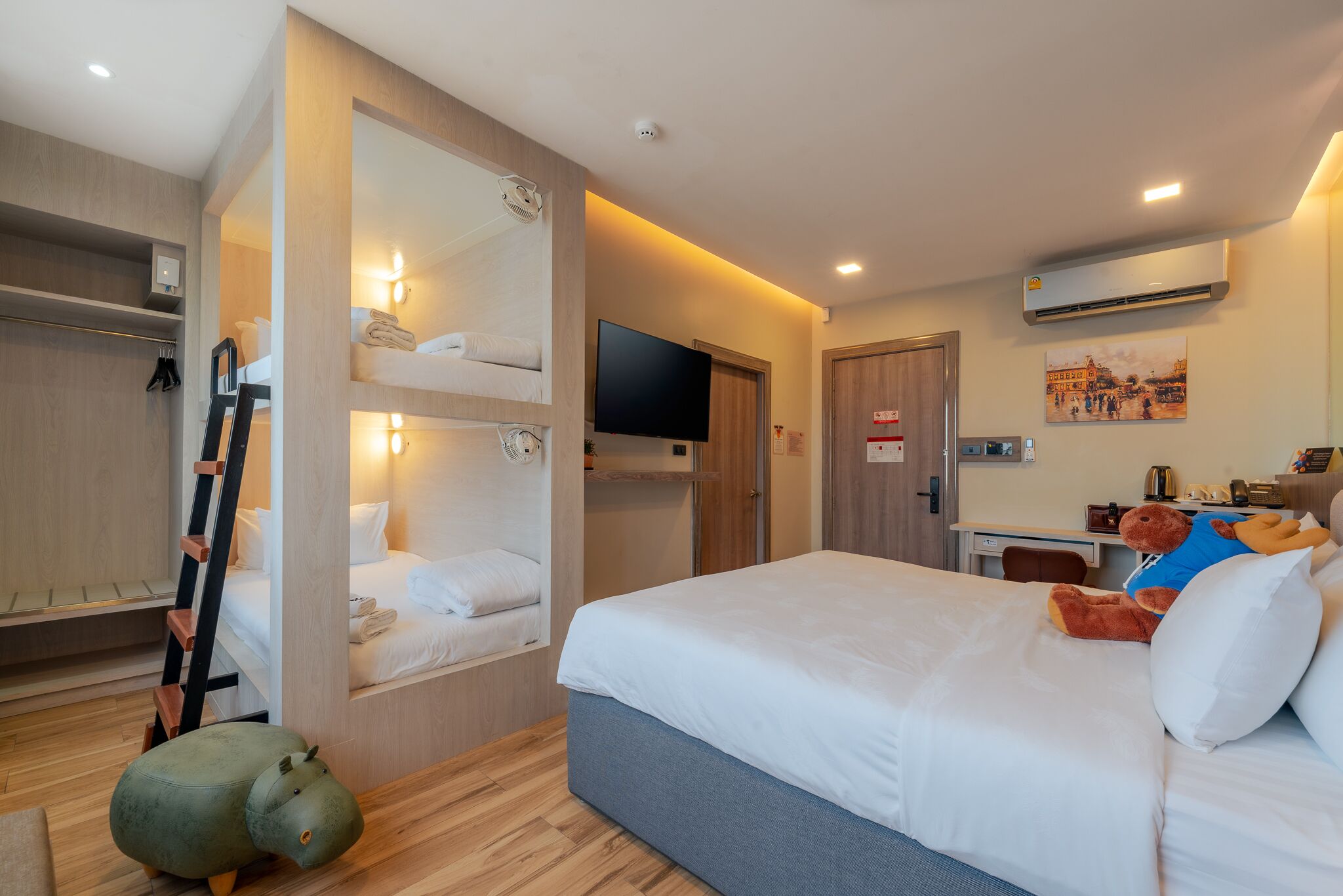 Una habitación de hotel con literas, un escritorio, una televisión y un osito de peluche.