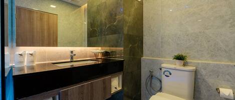 Un baño moderno con encimera negra, armarios de madera, pared de mármol y un inodoro con una toalla y una planta encima.