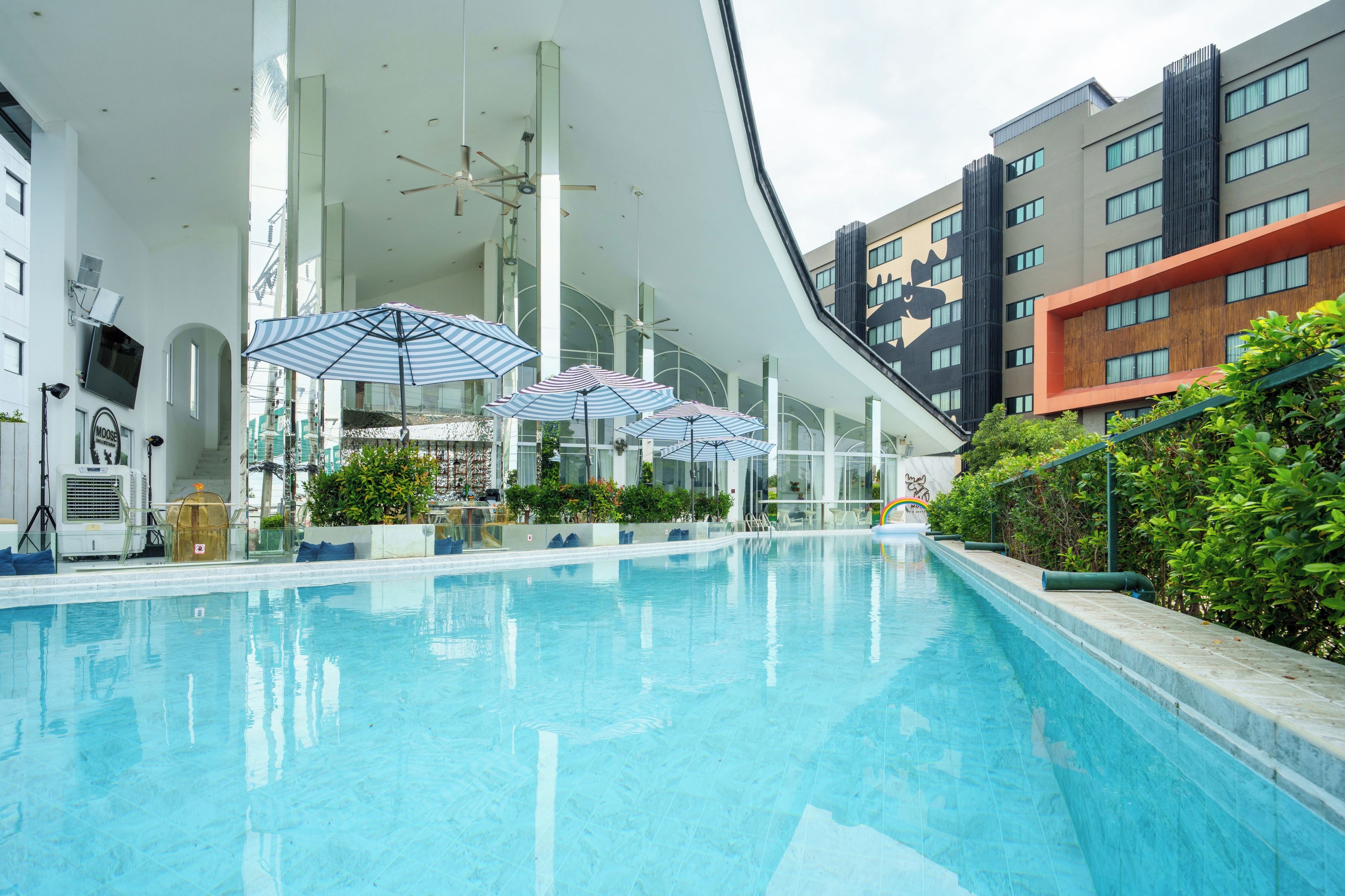 Una piscina con sombrillas, rodeada de edificios modernos con amplios ventanales y balcones.