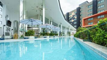 Una piscina con sombrillas, rodeada de edificios modernos con amplios ventanales y balcones.