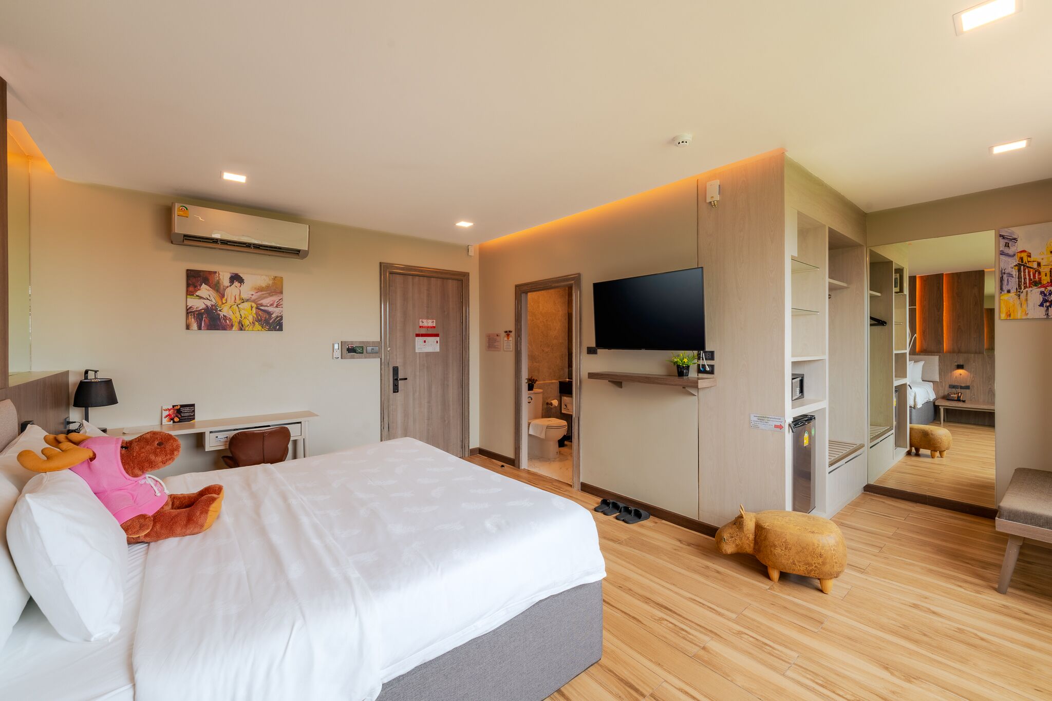 A modern hotel room with a large bed, a desk, a television, and a mirror.