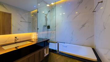 Un baño moderno con pared de mármol, ducha con cerramiento de vidrio, tocador de madera y bañera blanca.