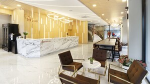 Eine moderne Hotelhalle mit einer Rezeption, einer Sitzecke und einer Treppe zu den oberen Etagen.