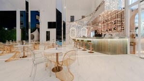 Ein modernes Interieur mit klaren Glastischen und -stühlen, einem Barbereich mit Kupferarmaturen und Blick auf das äußere Gebäude.