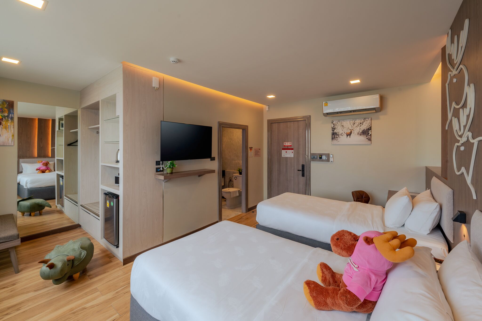 A hotel room with two beds, a TV, a mirror, and a small kitchenette.
