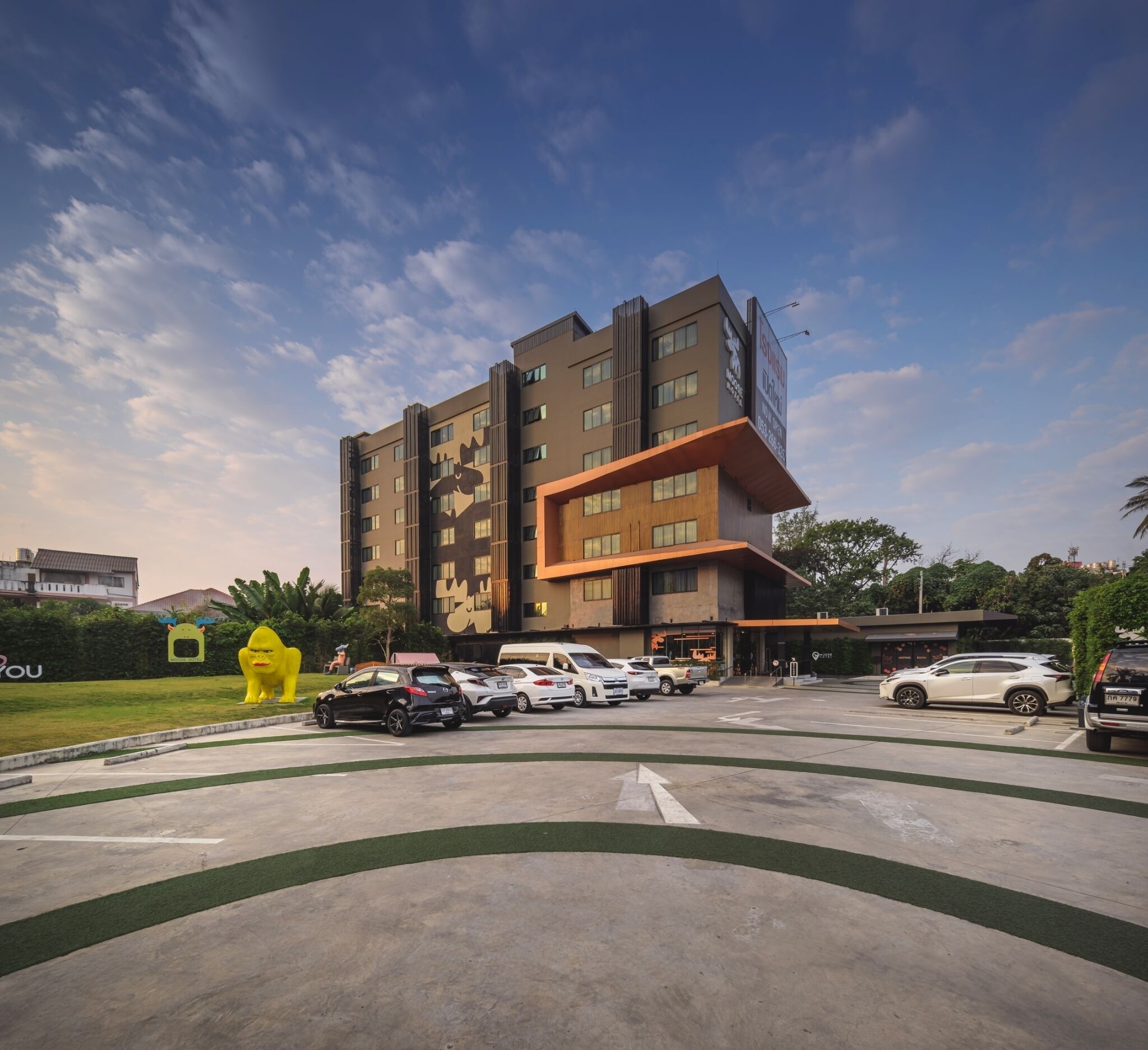 Un moderno edificio de varios pisos con un diseño arquitectónico único, destacando una entrada imponente y un estacionamiento con varios automóviles.