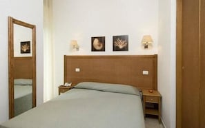 A hotel room with a wooden headboard, a bed with a grey bedspread, two bedside tables with lamps, and three framed pictures on the wall.