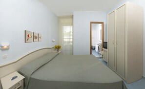 A bedroom with a bed, a nightstand, a TV, a wardrobe, and a bathroom visible through an open door. - Hotel Belmar (Cattolica)