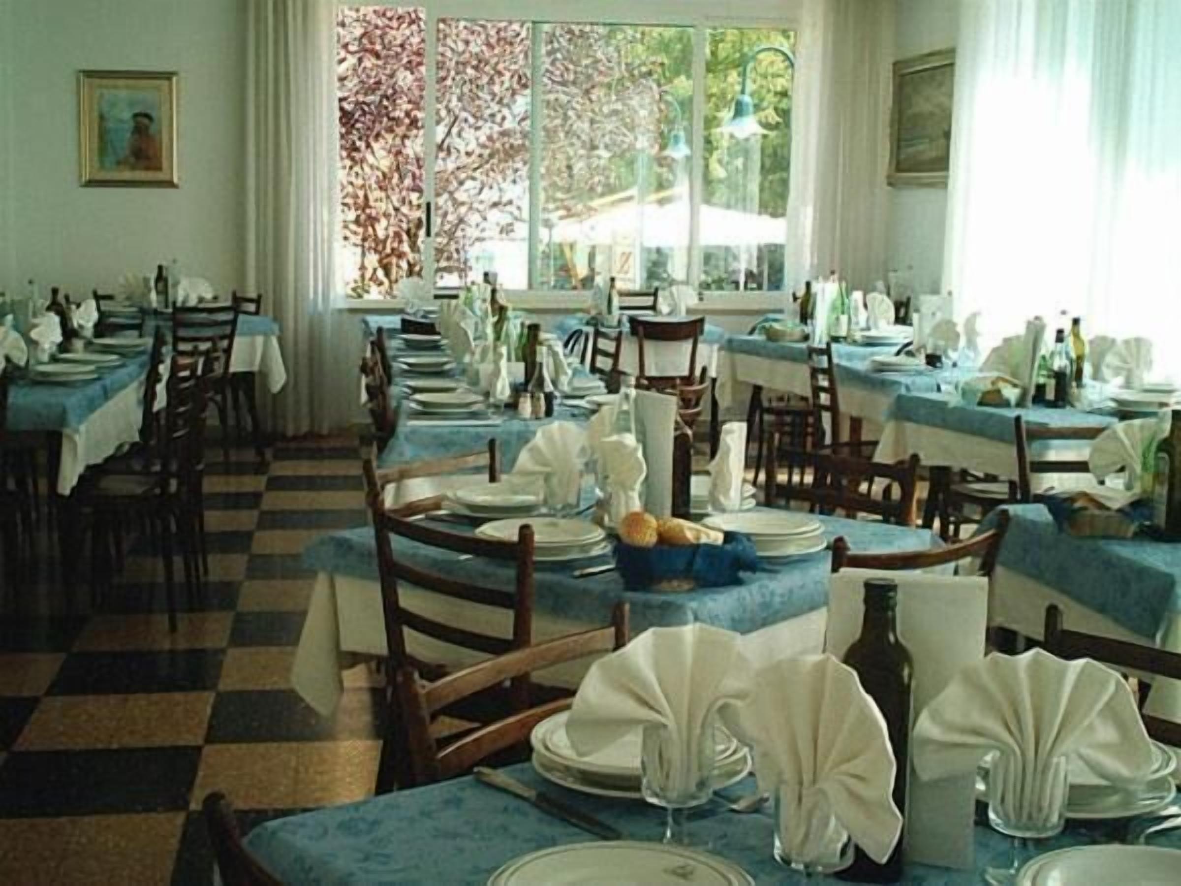A dining area with multiple tables set for service, a checkered floor, and large windows with curtains.