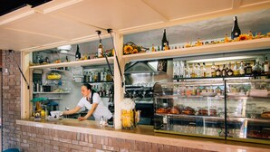 Eine Bar mit Regalen voller Spirituosenflaschen, einer Kaffeemaschine und einer Vitrine mit Gebäck.