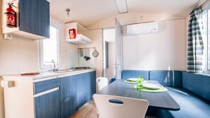 Eine kleine Küchenzeile mit Herd, Spüle und Stauraumschränken. Angrenzend befindet sich ein Essbereich mit Tisch und Stühlen.