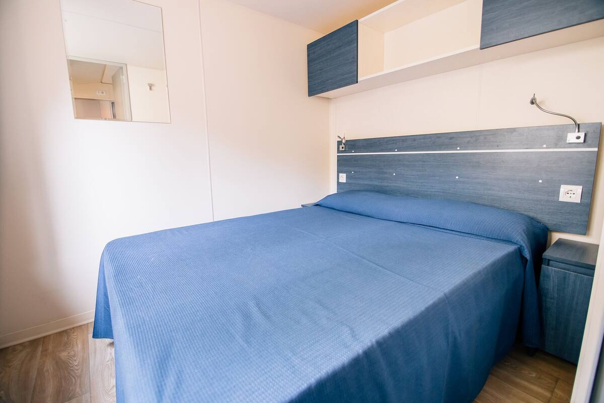 Ein Einzelbett mit blauer Bettdecke in einem Zimmer mit Holzboden und weißer Wand.