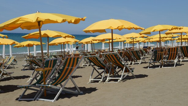 Ein Strand mit mehreren Reihen gestreifter Liegen und gelber Sonnenschirme.