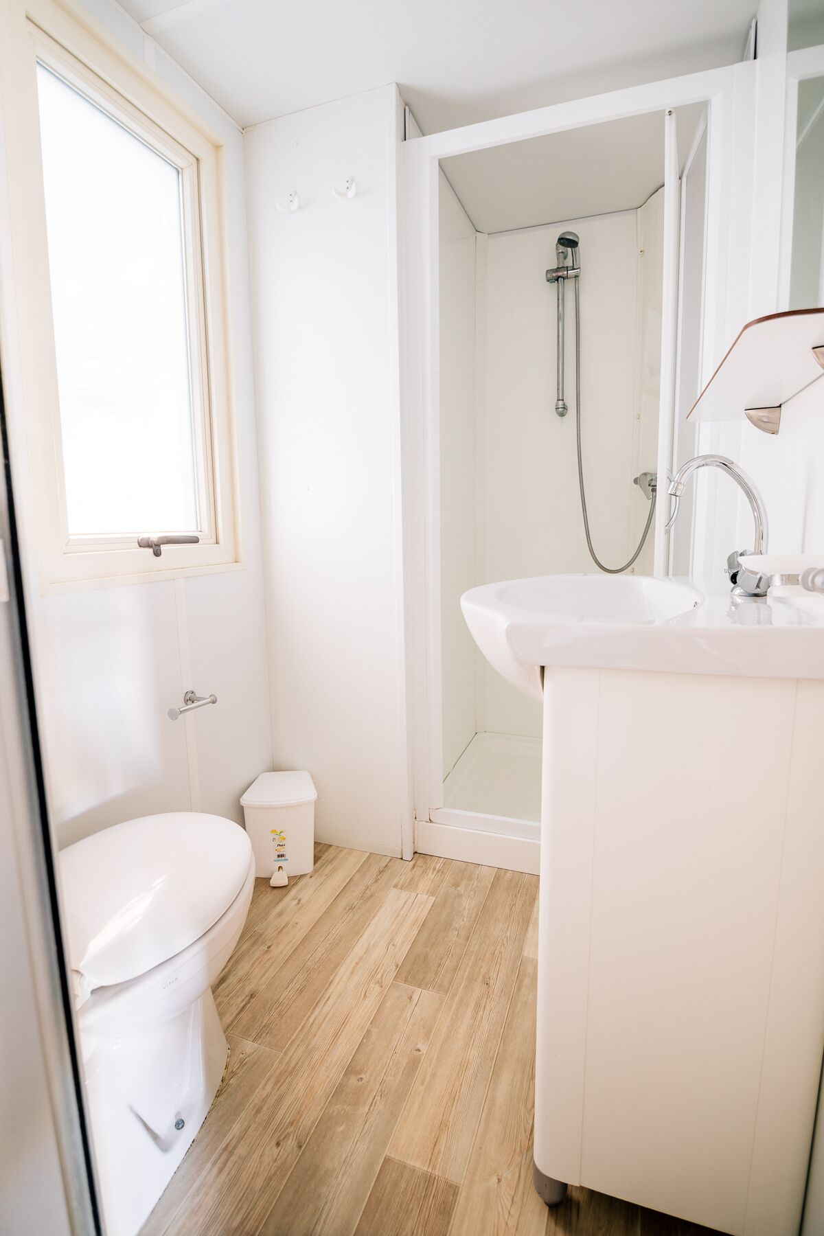 Ein modernes Badezimmer mit Toilette, kleinem Mülleimer, Duschbereich und Waschbecken.
