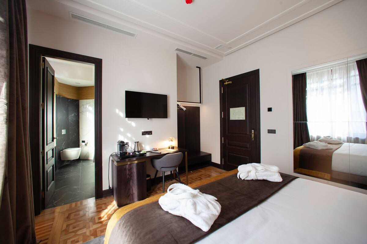Une chambre d’hôtel avec un lit, un bureau, une chaise, une télévision et une salle de bain visible à travers une porte ouverte.