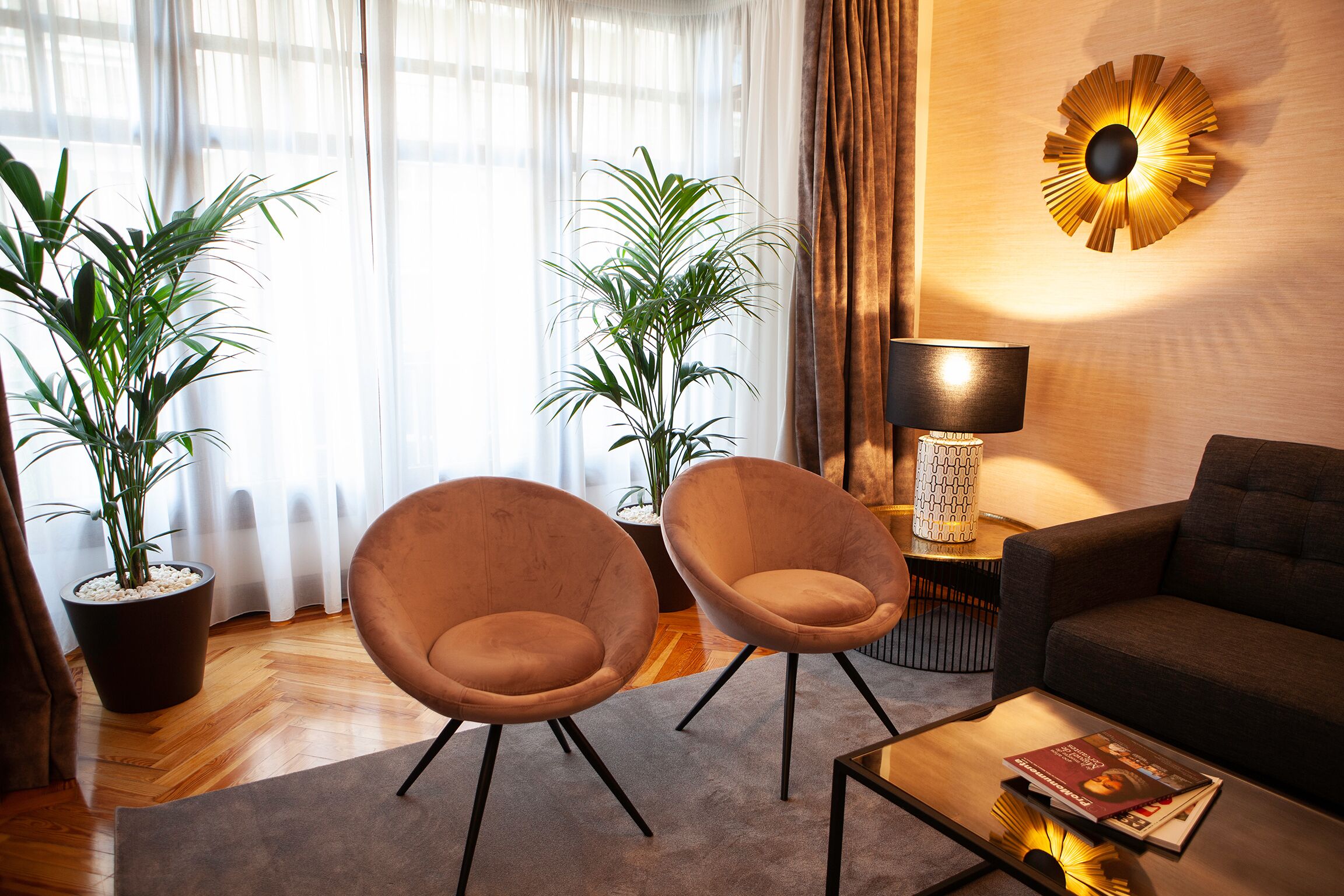 Un salon moderne avec deux fauteuils, un canapé, une table basse et un lampadaire. On y trouve également deux plantes en pot et une grande horloge murale.