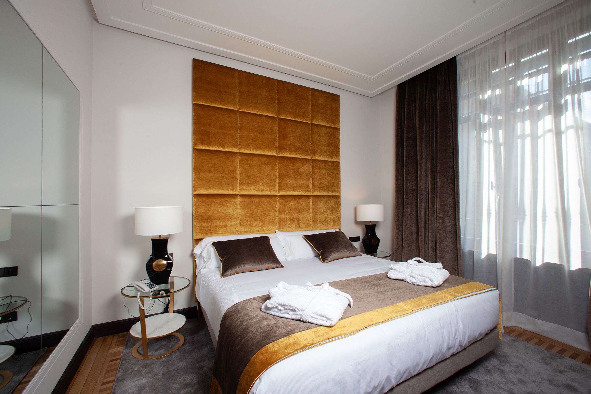 Habitación de hotel con una cama grande, dos mesitas de noche, un espejo y una ventana con cortinas.