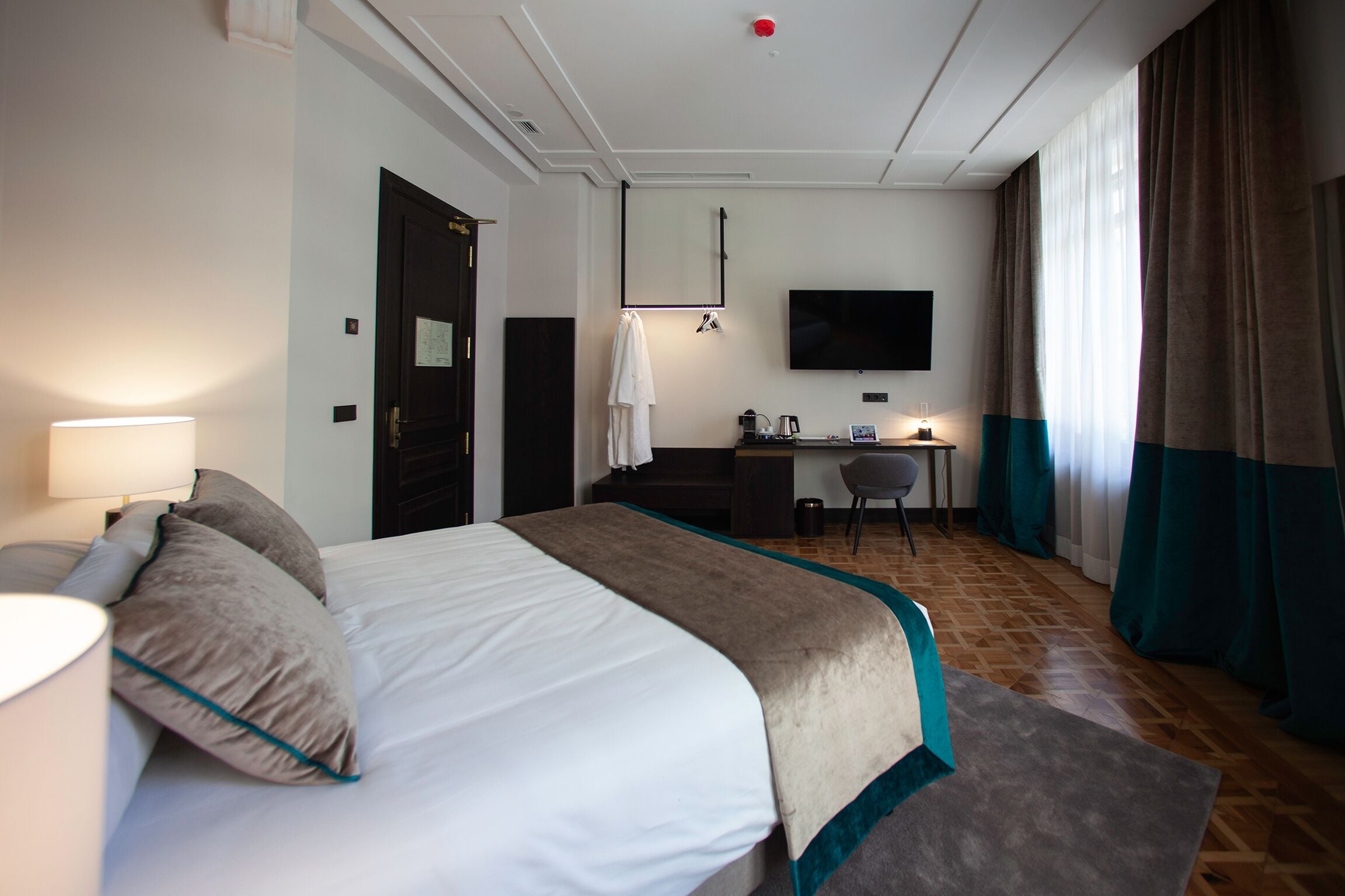 Una habitación de hotel con cama, escritorio, silla, televisor y lámpara.