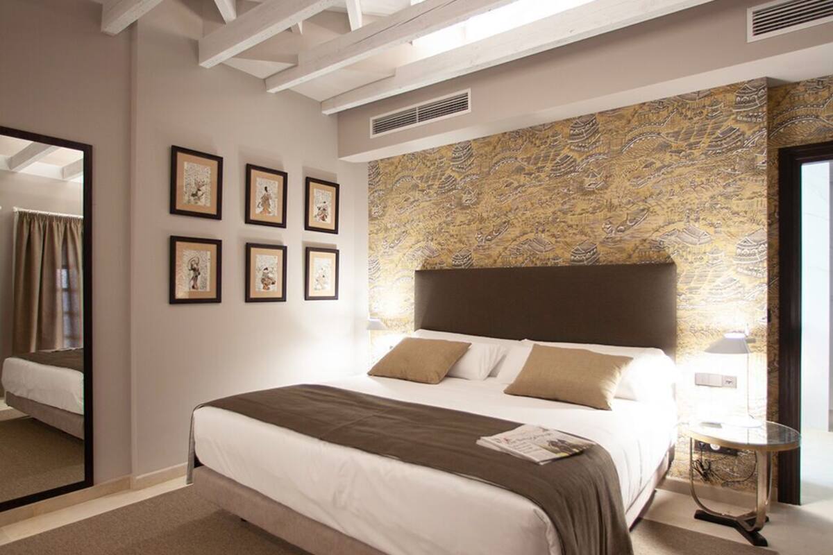 Une chambre avec un grand lit, un miroir, des tableaux encadrés accrochés au mur et un mur à texture.