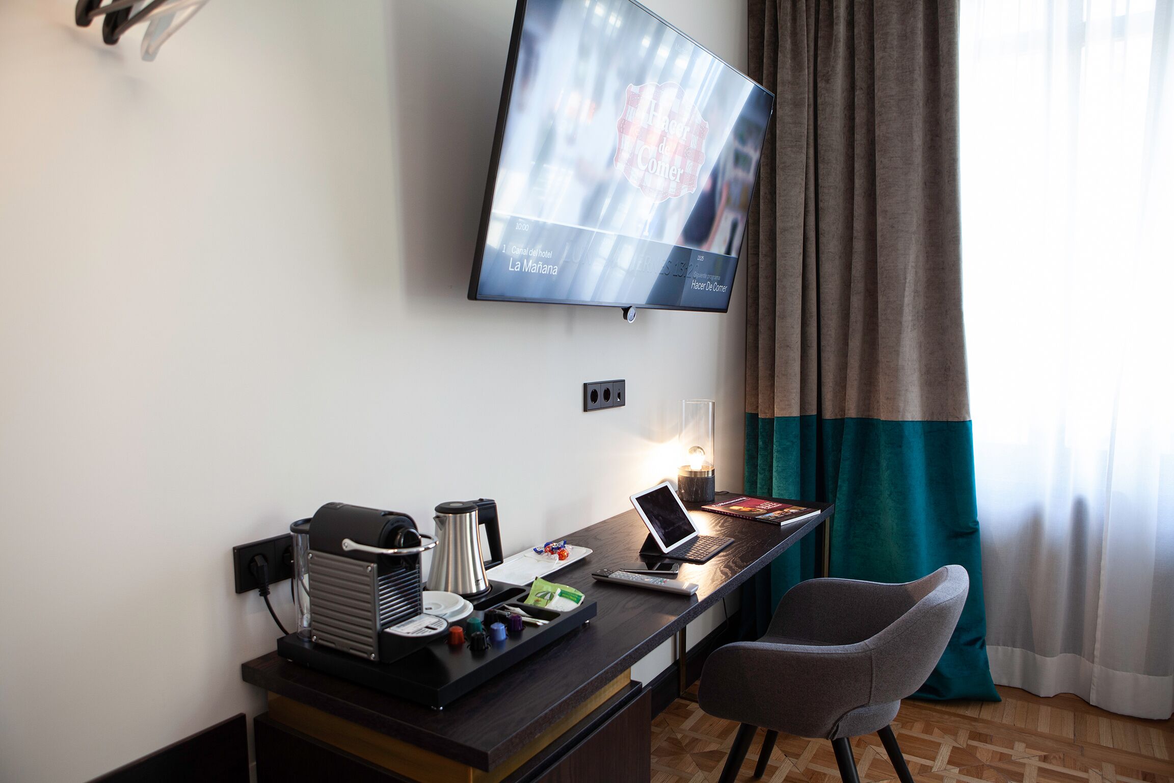 A hotel room with a desk, a laptop, a coffee maker, and a TV mounted on the wall.