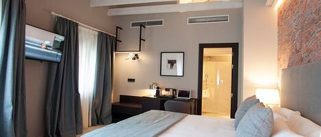 A modern hotel room with a large bed, a desk, a flat-screen TV, and a bathroom visible through an open door.