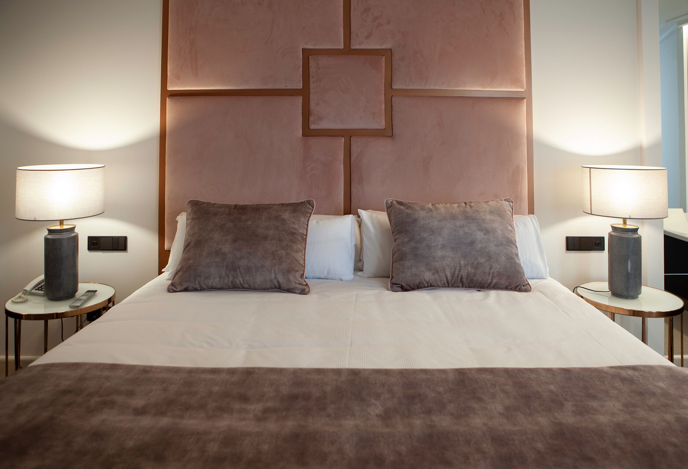 A neatly made bed with two pillows, a bedside table with a lamp, and a wall panel design.