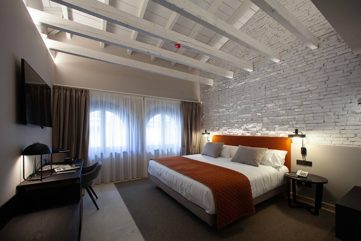 Une chambre d’hôtel avec un lit, un bureau, une chaise, une table de chevet et un mur en briques.