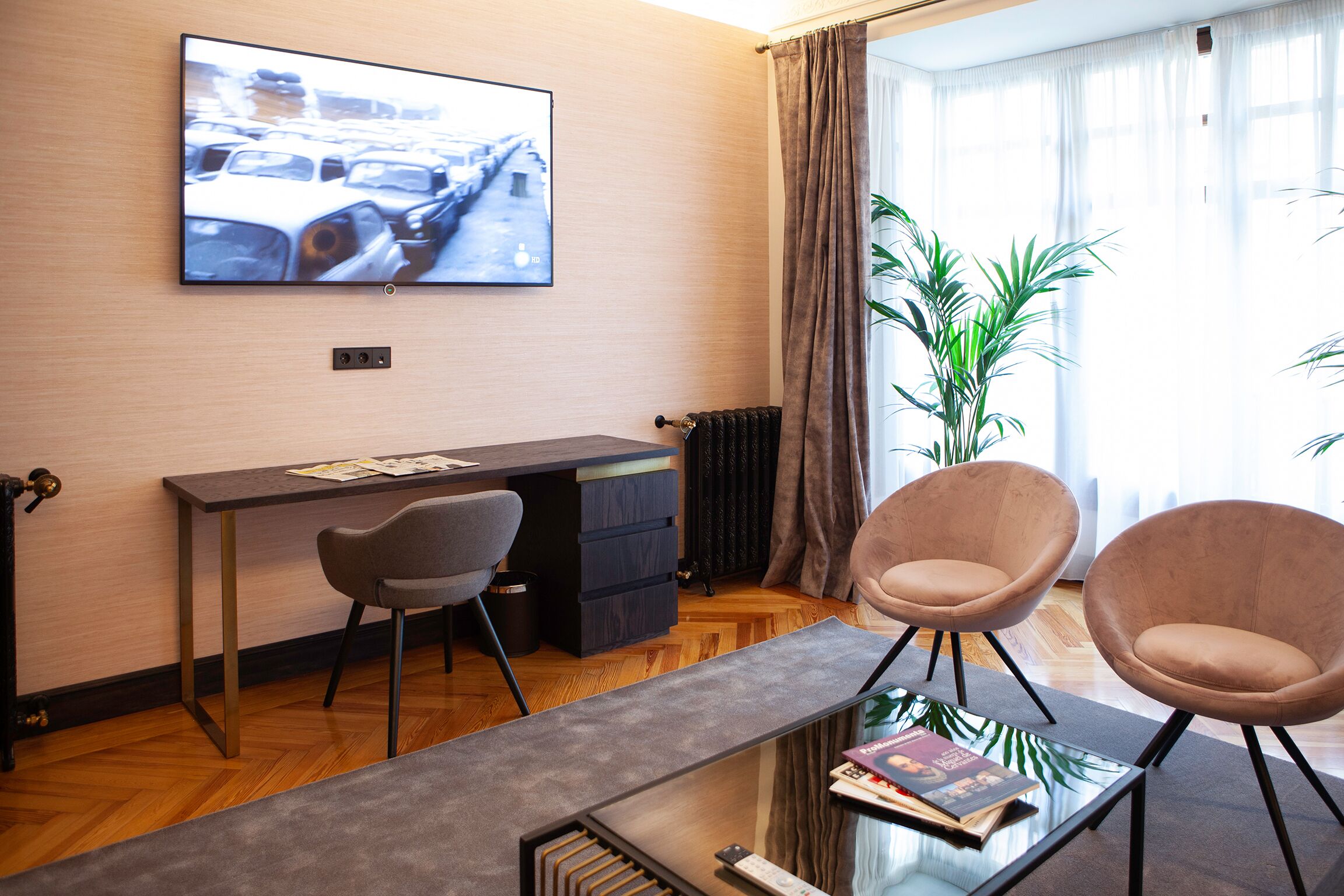 Una habitación moderna con escritorio, dos sillas, televisión y un amplio ventanal con cortinas.