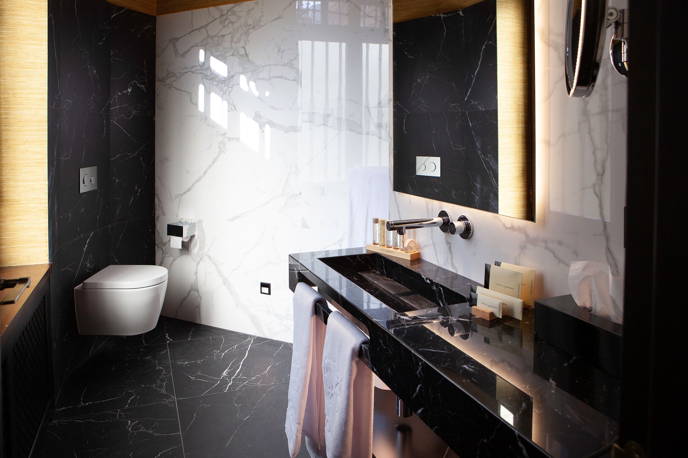 Un baño moderno con tocador de mármol negro, inodoro y espejo grande.