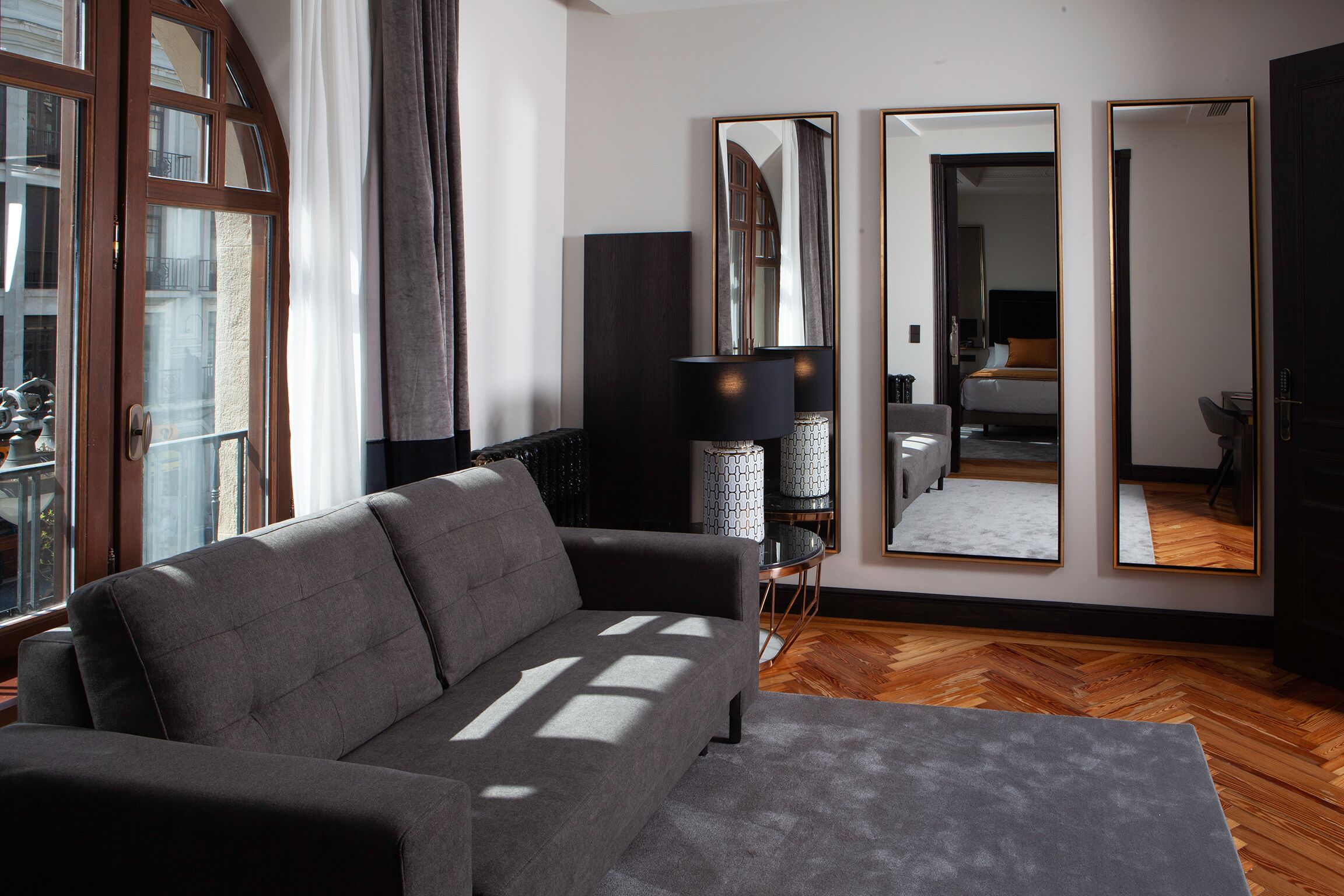 Una sala de estar moderna con un sofá gris, un espejo grande y suelo de madera.