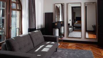 A modern living room with a grey sofa, a large mirror, and a wooden floor.