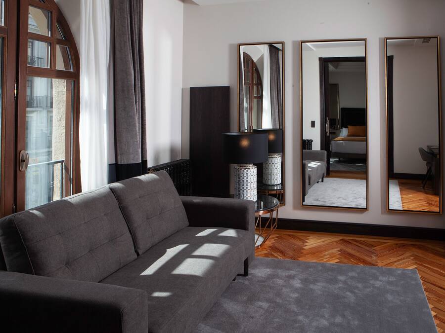 Una sala de estar moderna con un sofá gris, un espejo grande y suelo de madera.