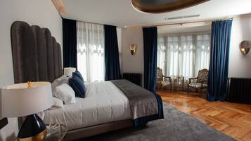 Habitación de hotel moderna con una cama grande, un área de descanso con dos sillones y vistas al exterior a través de amplios ventanales.